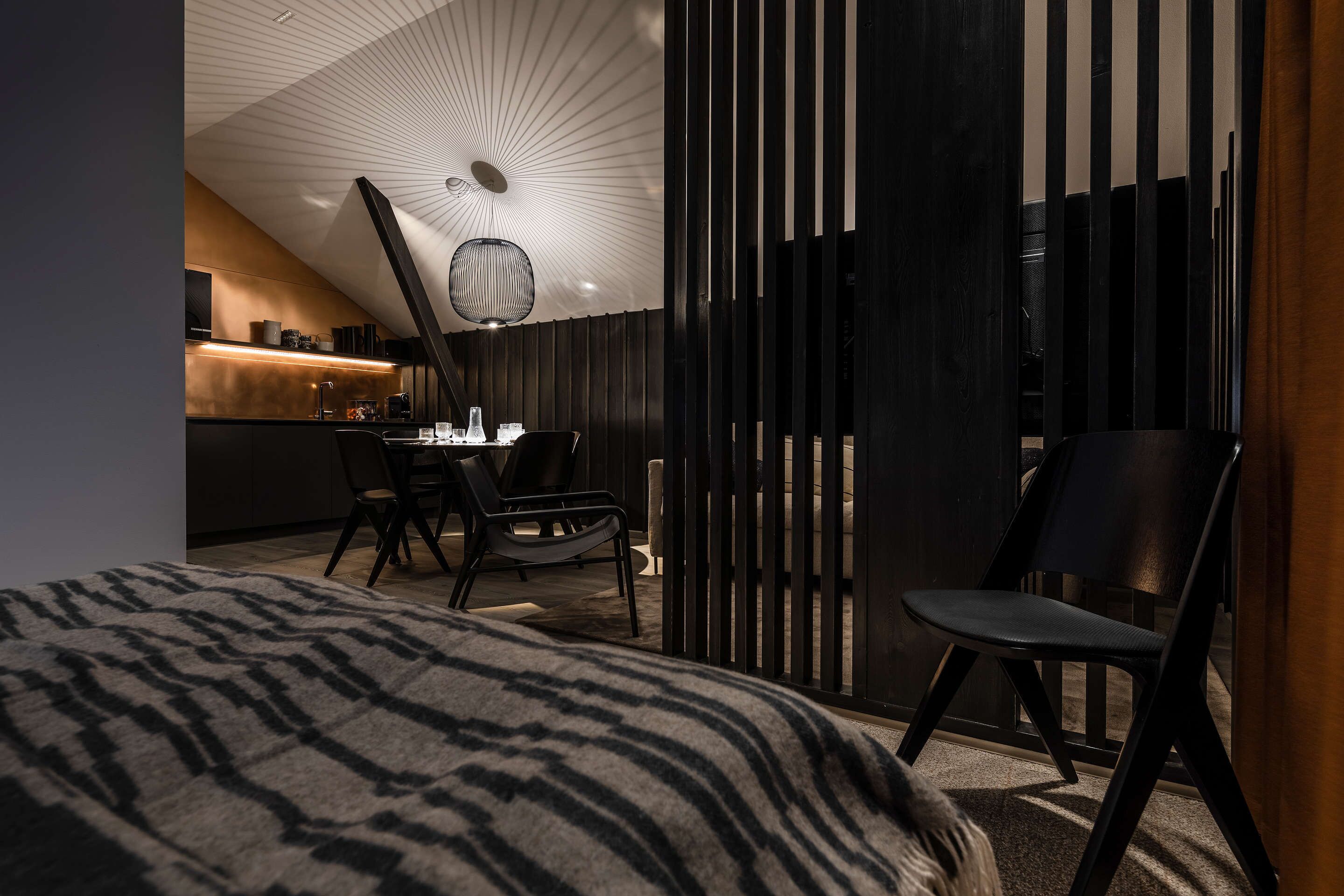 Moderni hotellihuone, jossa on sänky, työpöytä ja tuoli. Taustalla näkyy keittiöalue.