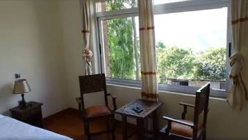 Une chambre d’hôtel avec un lit, une chaise, une petite table et une fenêtre avec des rideaux.