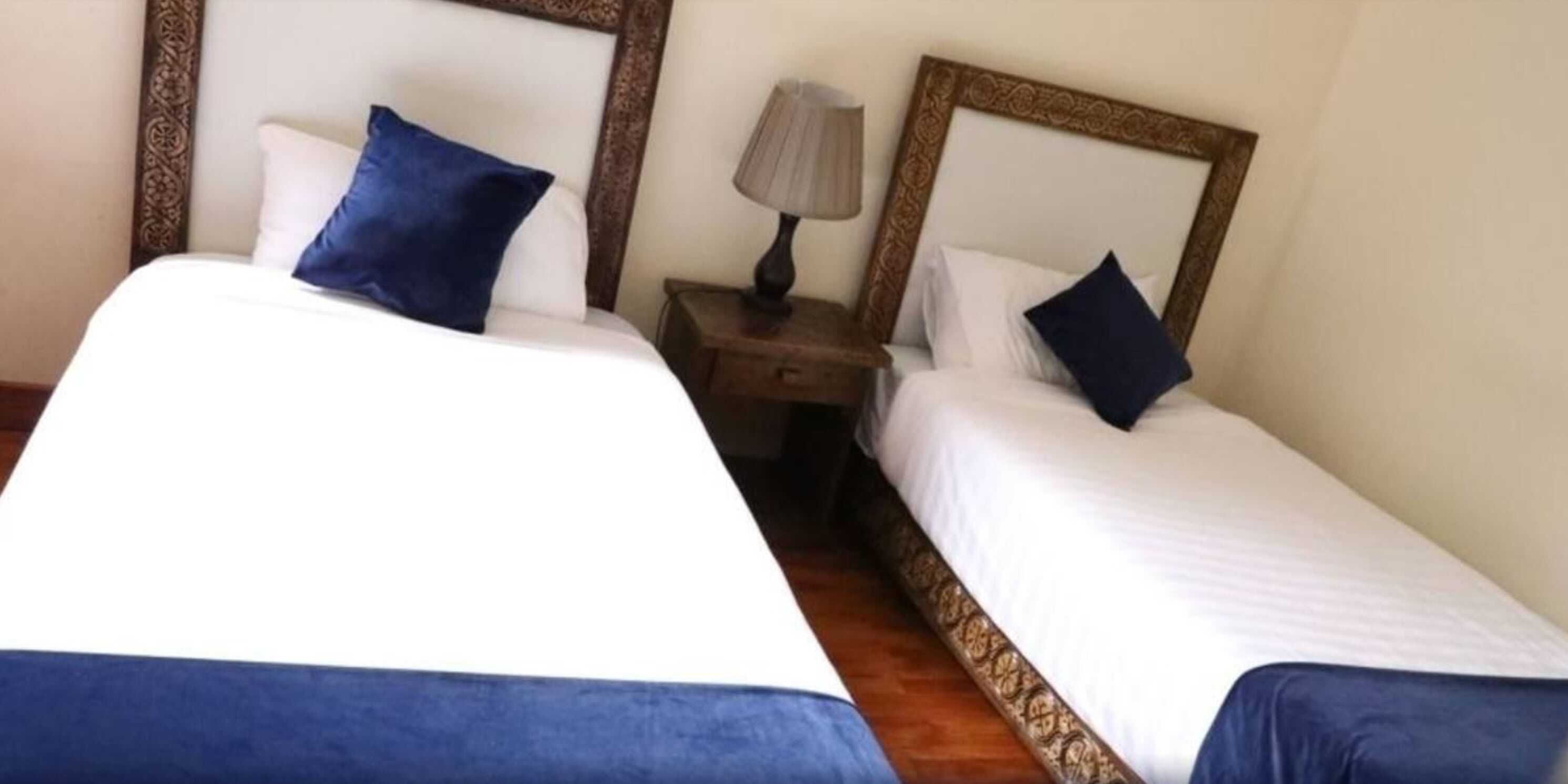 Two single beds with matching headboards, a bedside table with a lamp, and a wooden floor.