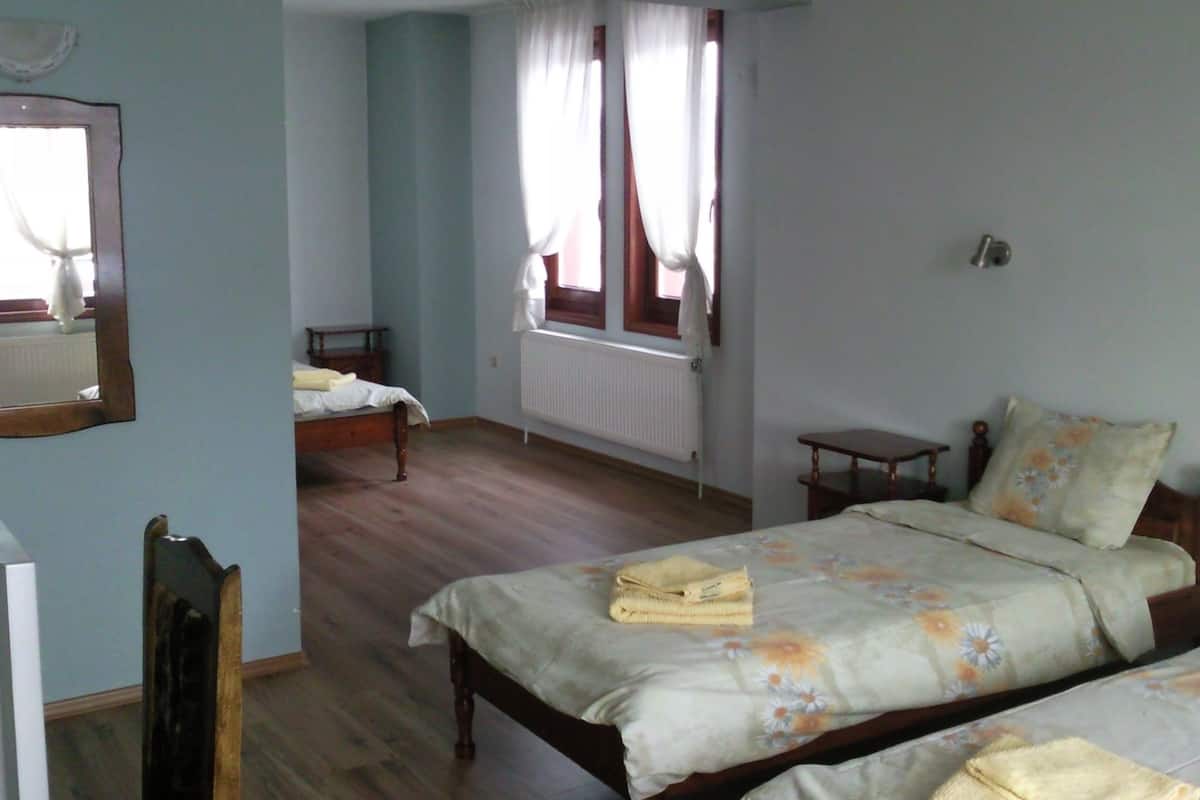 A bedroom with two beds, a wooden floor, a radiator, and a window with curtains.