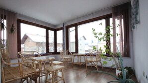 A spacious room with large windows, wicker furniture, and potted plants. - Ilinden (Bansko)