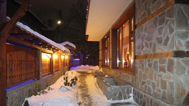A snow-covered pathway leading to a stone building with wooden accents and illuminated windows. - Ilinden (Bansko)
