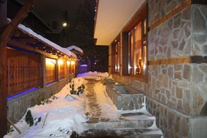 Un sendero cubierto de nieve que conduce a un edificio de piedra con detalles de madera y ventanas iluminadas.