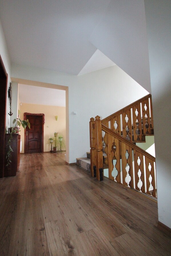 Una escalera de madera con barandal blanco, una puerta de madera al pie y un pasillo con suelo de madera.