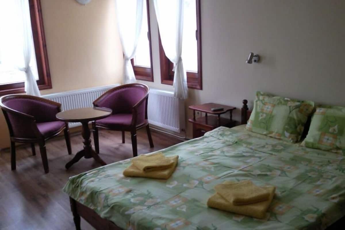 A room with a bed, two chairs, a small table, and a window with curtains.
