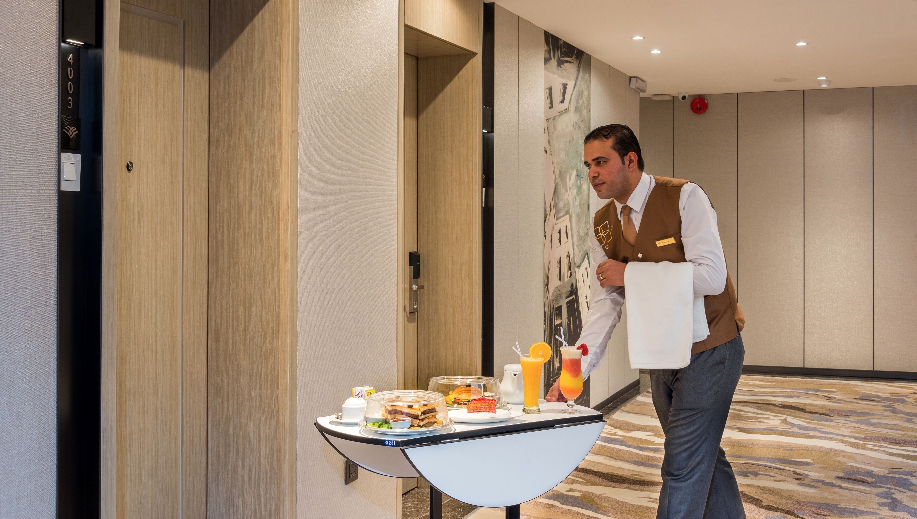 A hotel room with a minibar, a wall-mounted clock, and a door with a number plate.