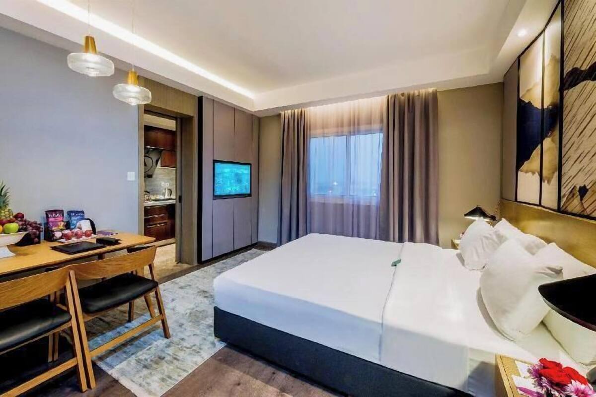 A hotel room with a bed, desk, chair, TV, and a fruit bowl.