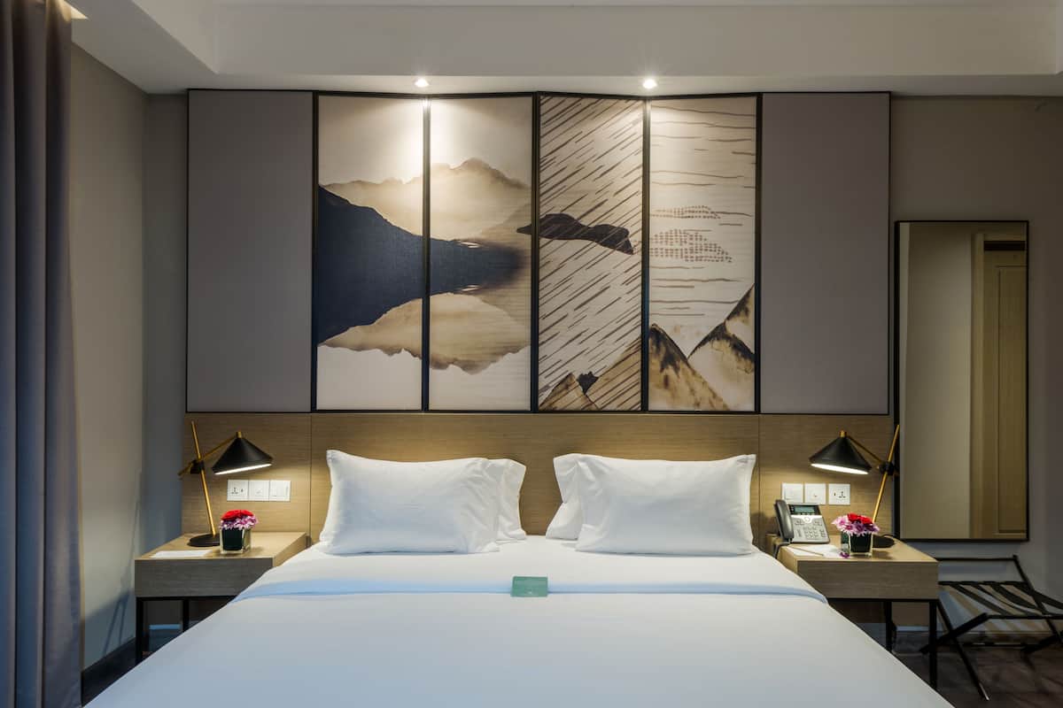 A hotel room with a large bed, two nightstands, a wall-mounted artwork, and a mirror.