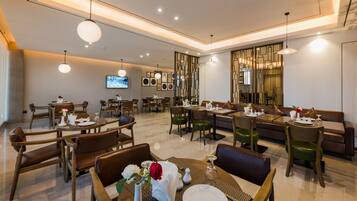 A modern dining area with multiple tables and chairs, a television mounted on the wall, and a decorative wall panel.