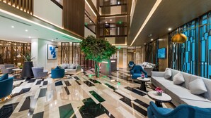 A spacious lobby with a modern design, featuring a large seating area, a reception desk, and a decorative tree. - Boudl Al Corniche (Dammam)