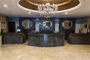 A hotel reception area with a marble counter, three large mirrors, and a chandelier. - Danube International Hotel (Qingdao)