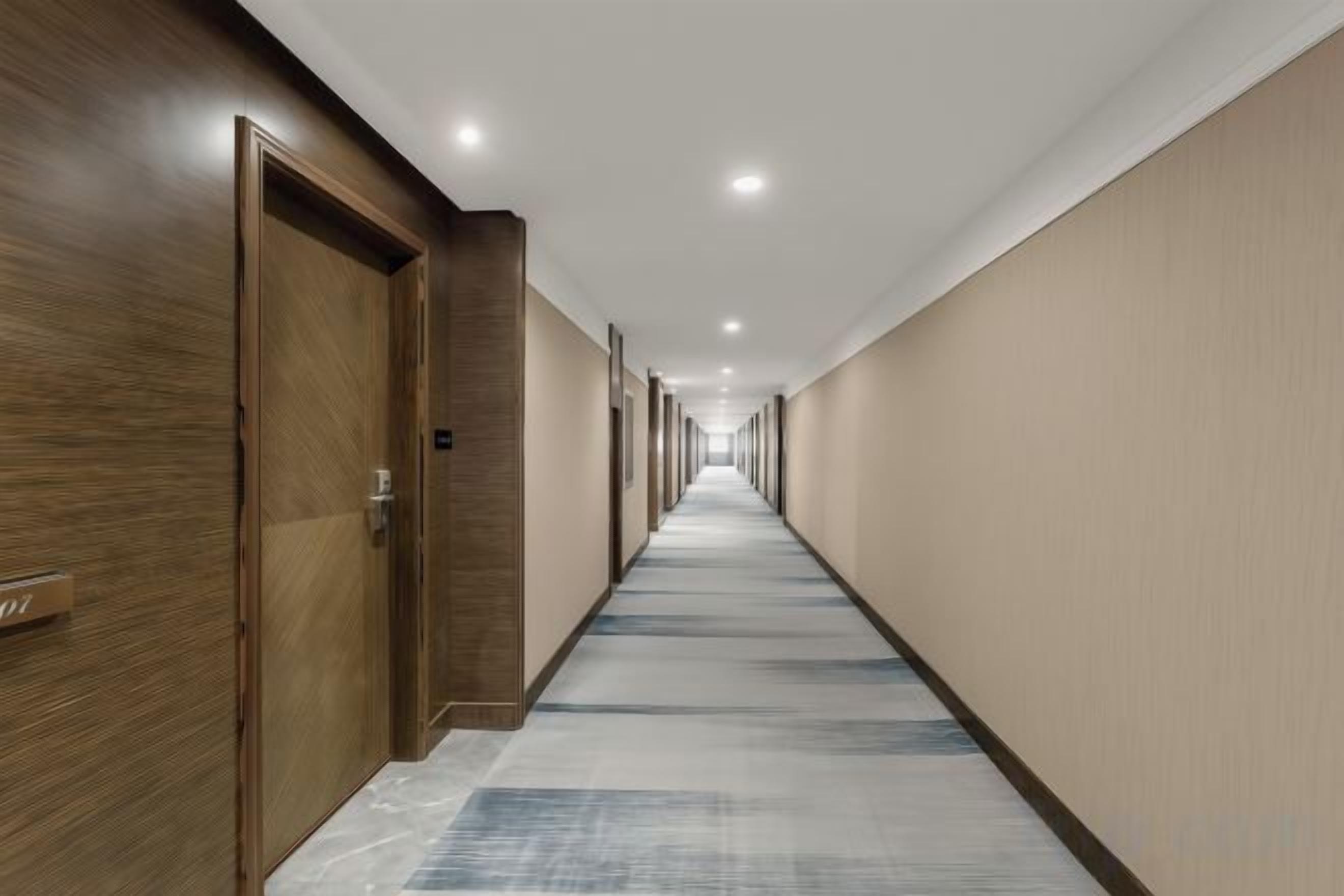 Un pasillo de hotel con puertas de madera, suelo alfombrado y una larga extensión.