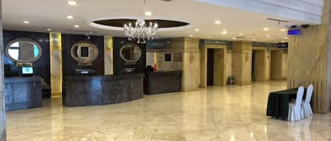 A hotel lobby with a reception desk, seating area, and a chandelier.