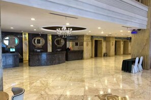 Un vestíbulo de hotel con recepción, zona de estar y una araña.