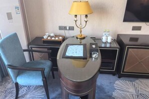 A hotel room with a desk, a chair, a lamp, a television, and a minibar. - Danube International Hotel (Qingdao)