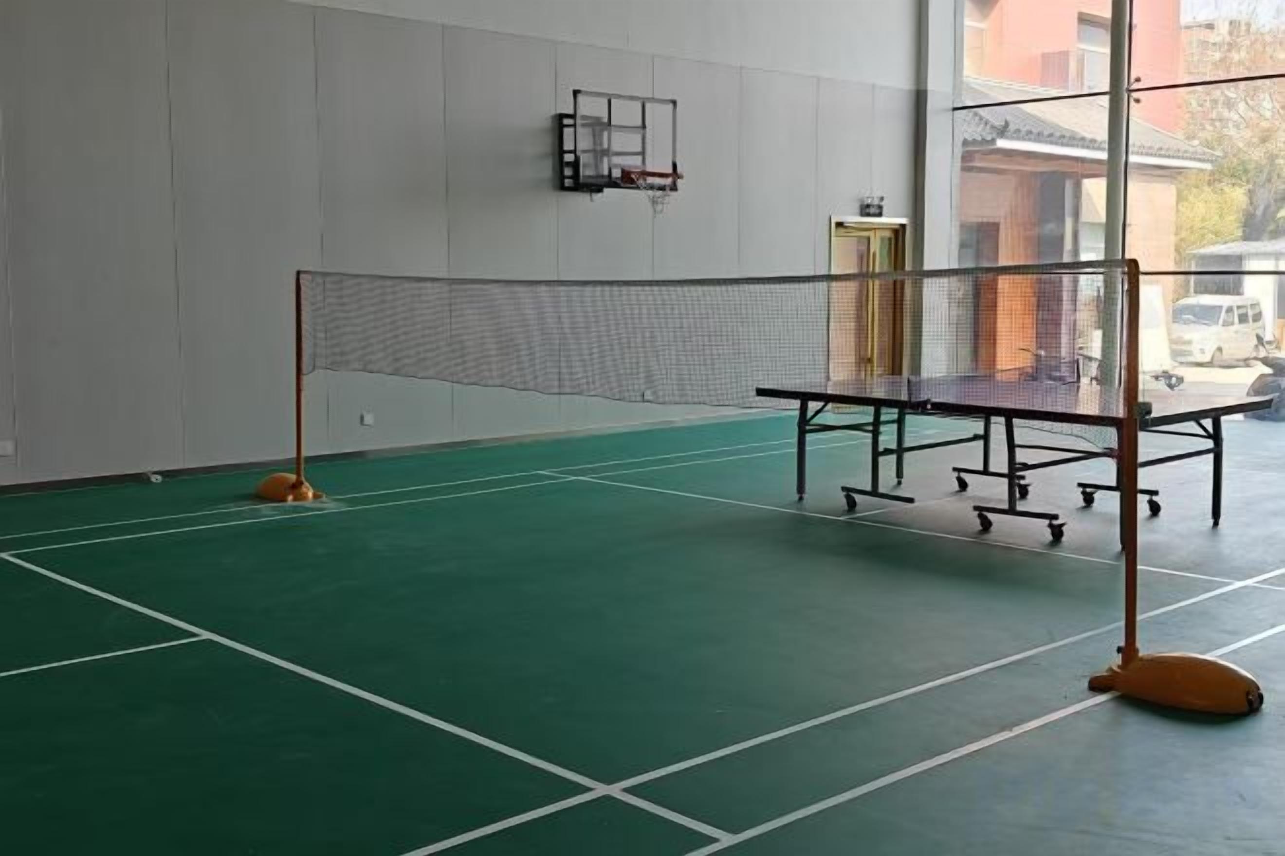 An indoor badminton court with a net, floor markings, and a wall-mounted rack.