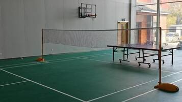 An indoor badminton court with a net, floor markings, and a wall-mounted rack.
