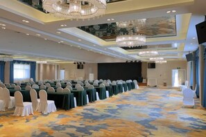 A conference room with rows of tables and chairs, a large screen, and a carpeted floor. - Danube International Hotel (Qingdao)