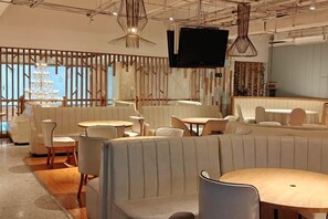 A modern restaurant interior with booths, round tables, and a flat-screen TV mounted on the wall. - Danube International Hotel (Qingdao)