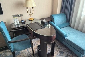 A hotel room with a sofa, a small table with a lamp, a chair, and a desk with a computer and a phone. - Danube International Hotel (Qingdao)
