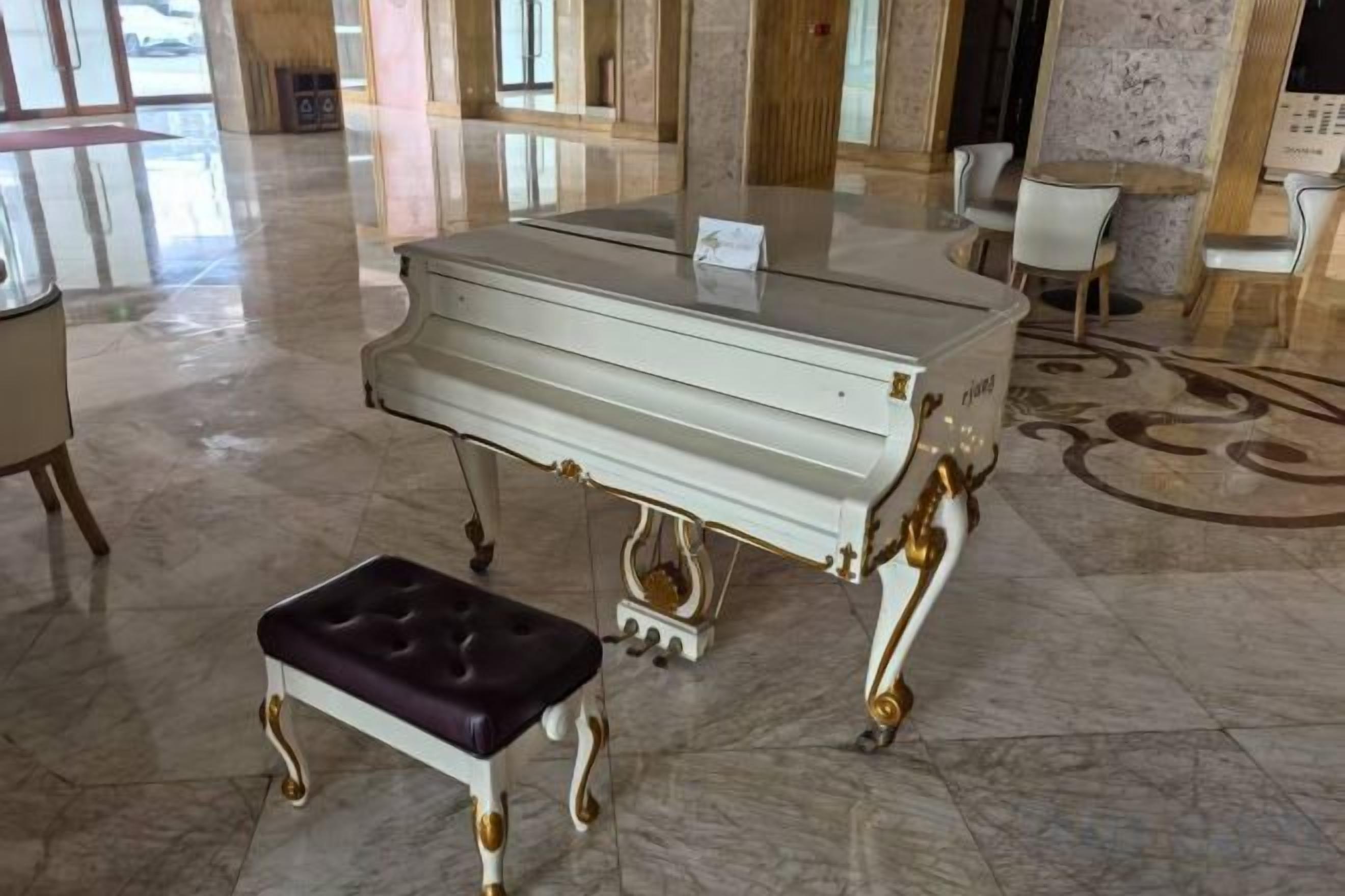 A grand piano in a spacious lobby with a marble floor and a plush bench.