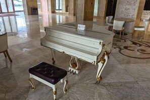 A grand piano in a spacious lobby with a marble floor and a plush bench. - Danube International Hotel (Qingdao)