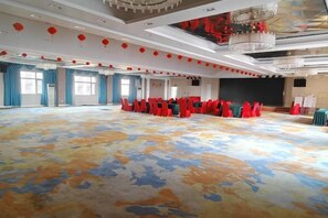 Een ruime zaal met rijen rode stoelen, een vloerbedekking en een kroonluchter.