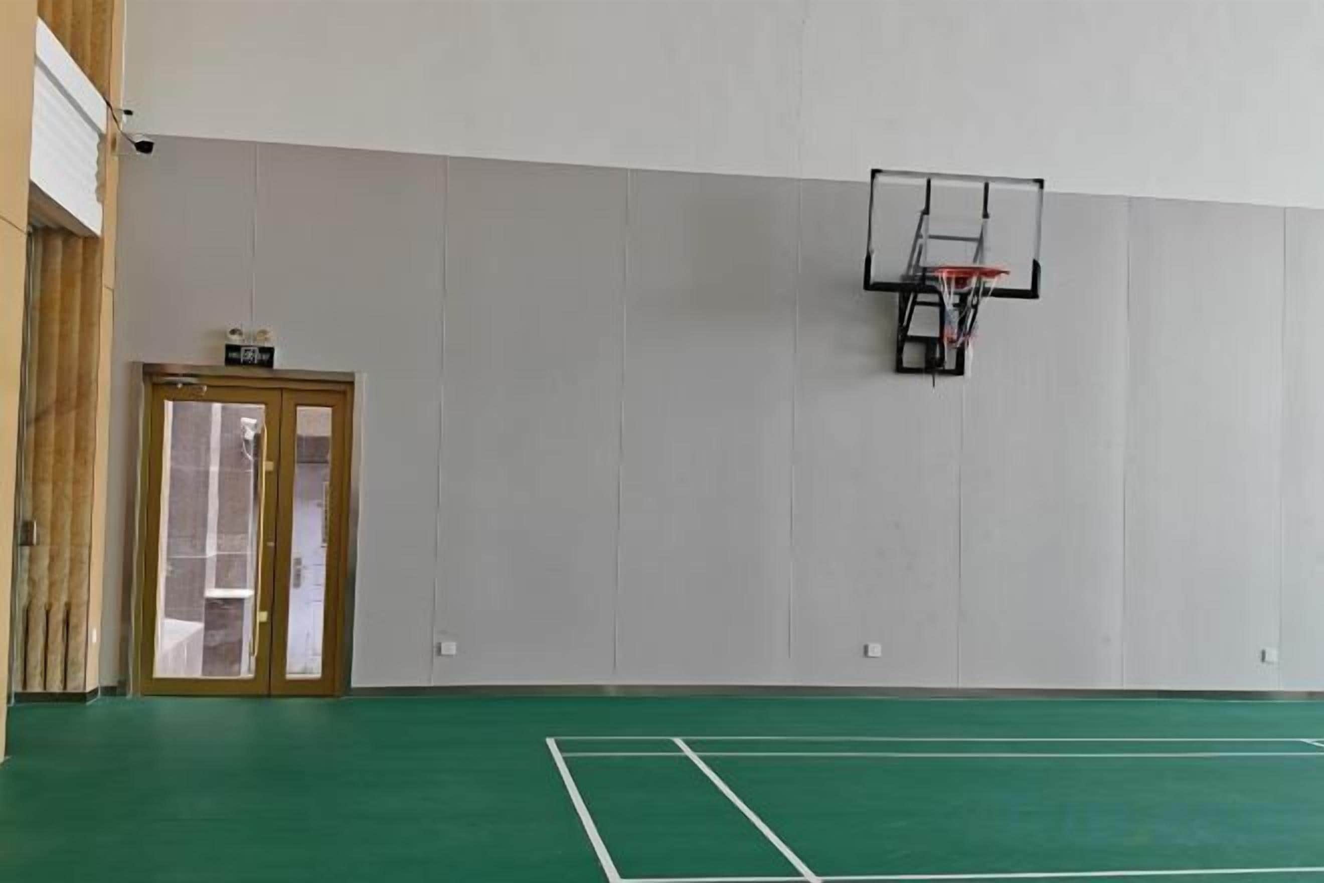 An indoor sports court with a basketball hoop, a door, and a wall-mounted sign.