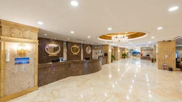 A hotel lobby with a marble floor, reception desk, and a chandelier.