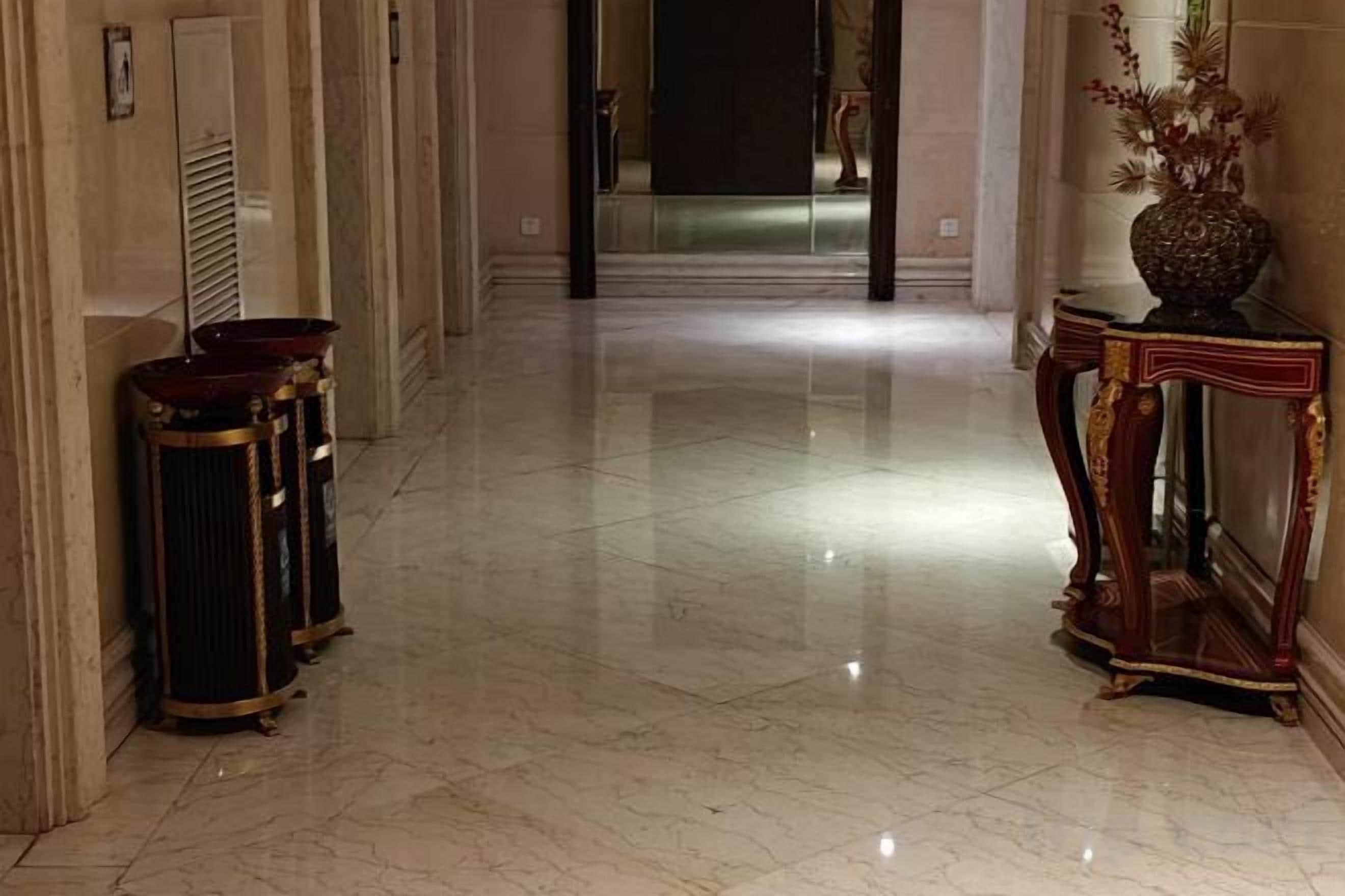 A marble-floored corridor with a grand entrance, a decorative vase, and a tall, ornate console table.