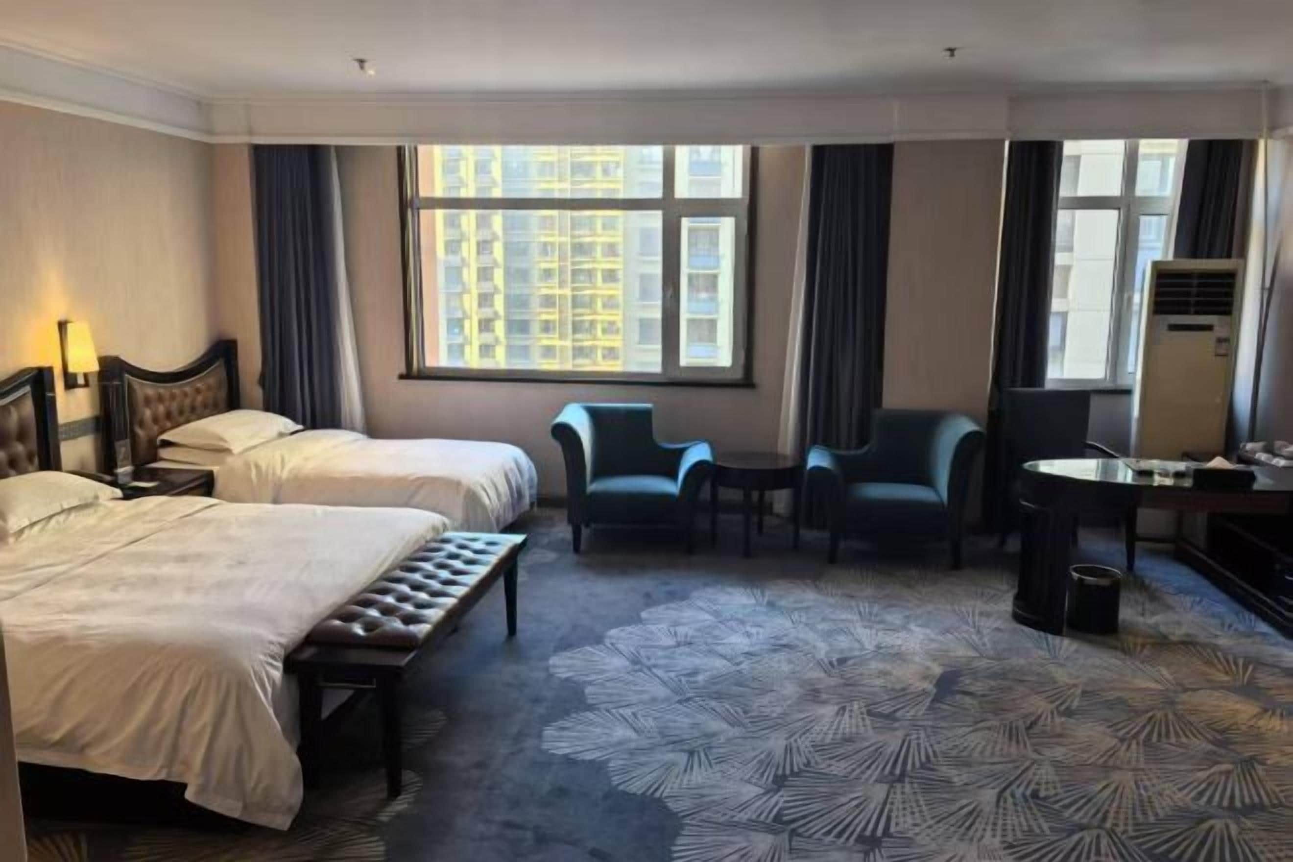Habitación de hotel con dos camas, un escritorio, una silla y un ventanal grande.