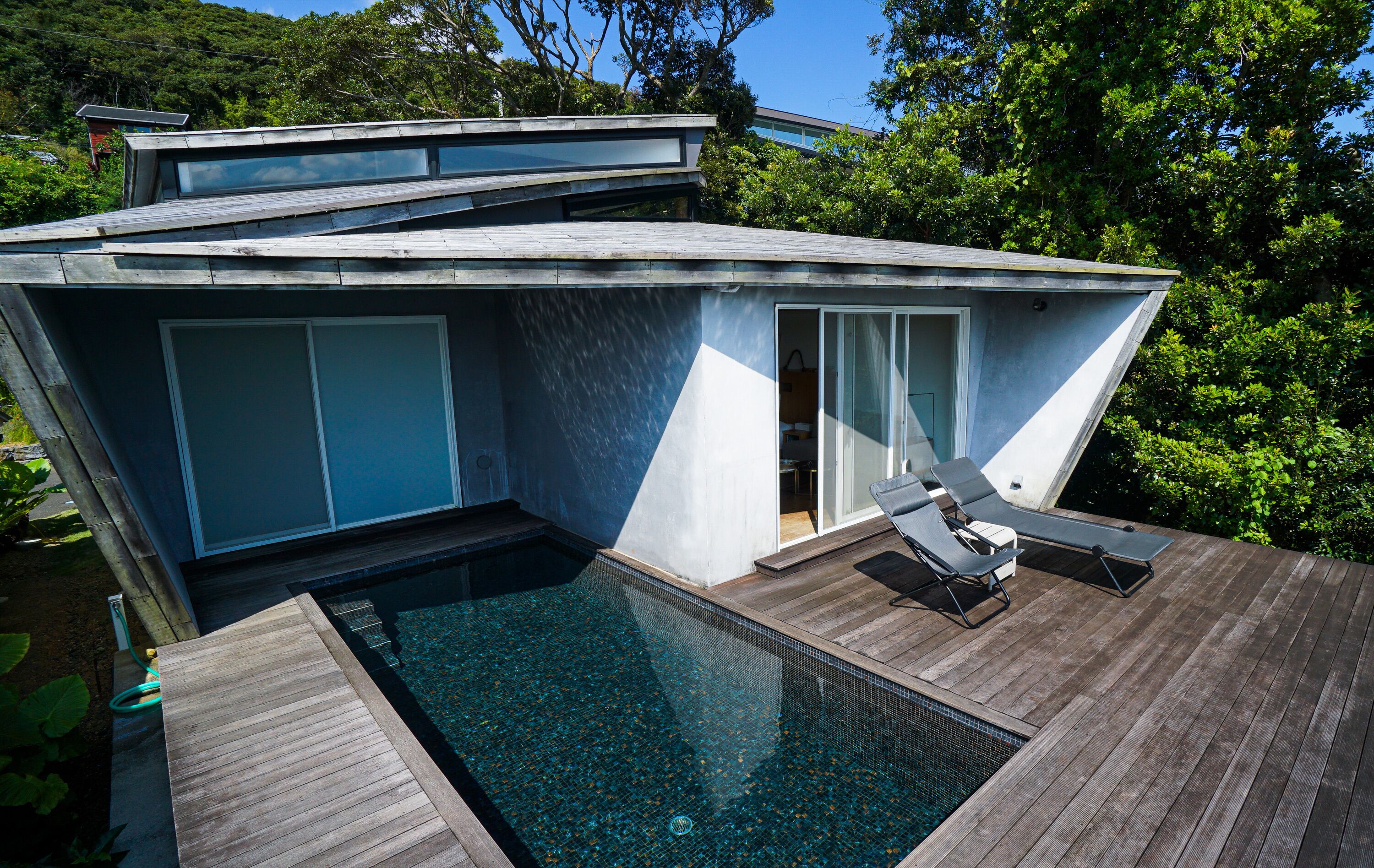 A modern house with a swimming pool, wooden deck, and a glass door leading to a covered outdoor area.