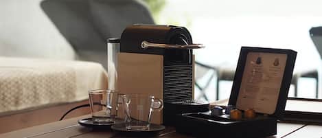 A coffee machine, two glasses, and a menu on a table in a room with a bed and a chair in the background.