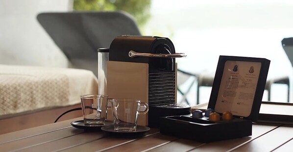 Una cafetera, dos vasos y un menú sobre una mesa en una habitación con una cama y una silla al fondo.