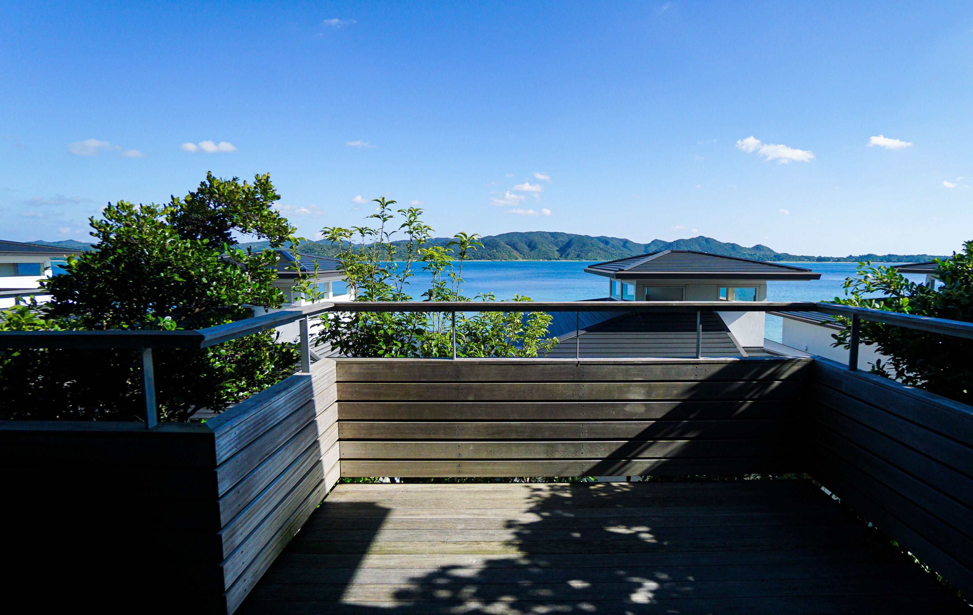 A wooden deck leading to a modern building with a view of the sea and mountains.
