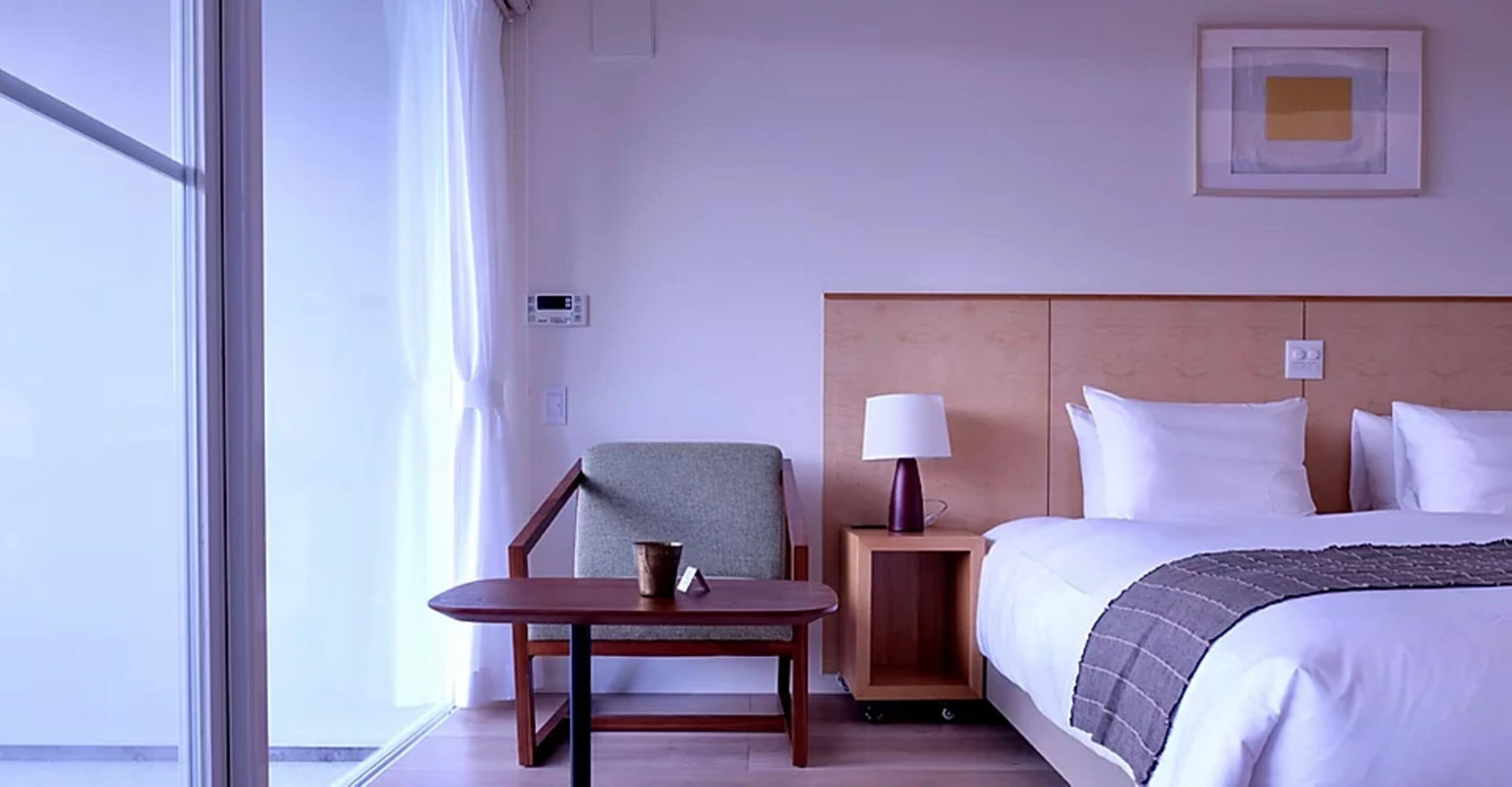 A hotel room with a bed, a nightstand, a table, a chair, and a window.