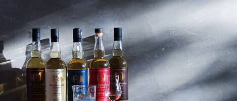 Varias botellas de whisky sobre una superficie reflectante, con una pared texturizada al fondo.