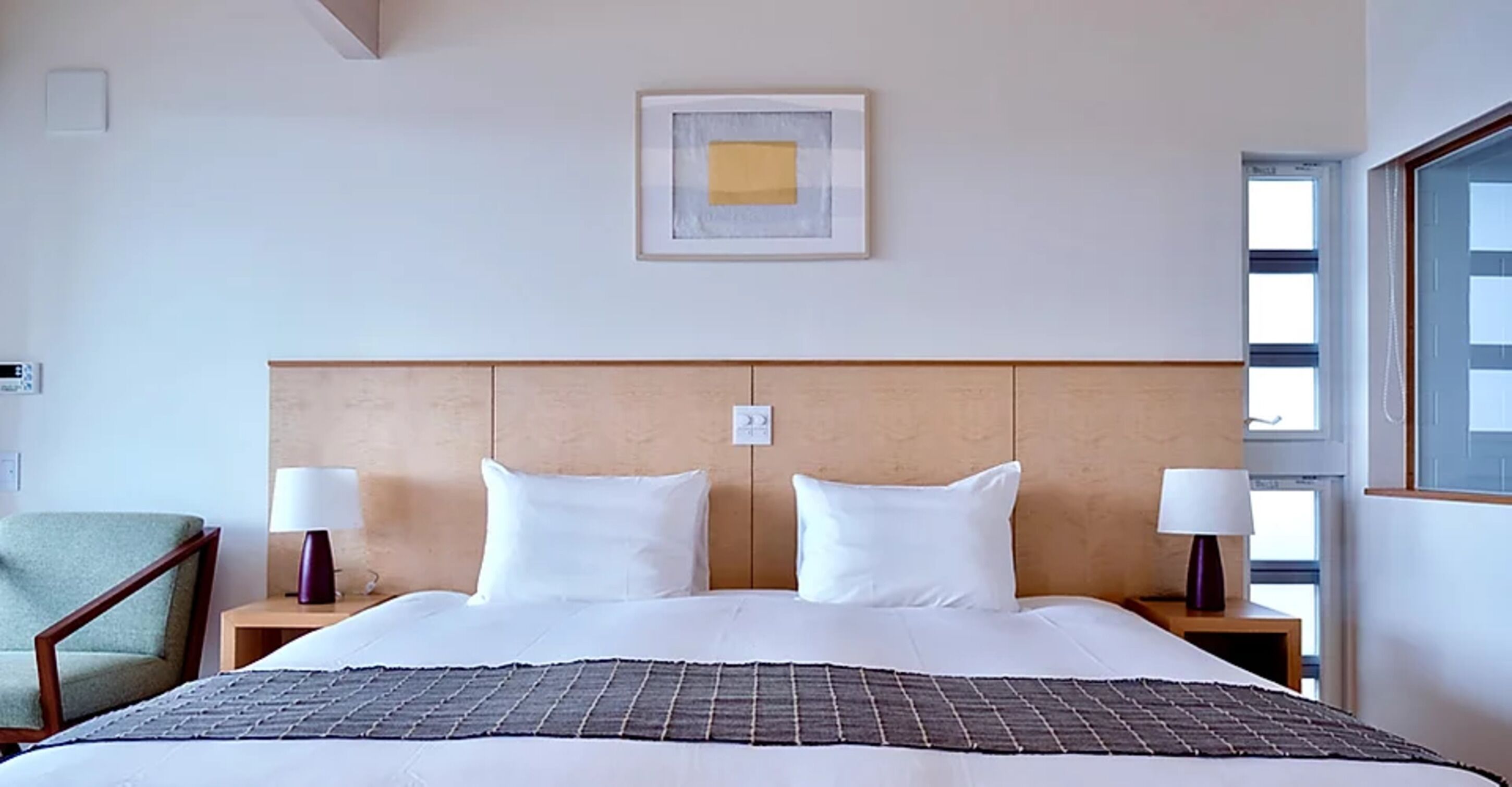 A hotel room with a large bed, two bedside tables, a chair, and a framed picture on the wall.