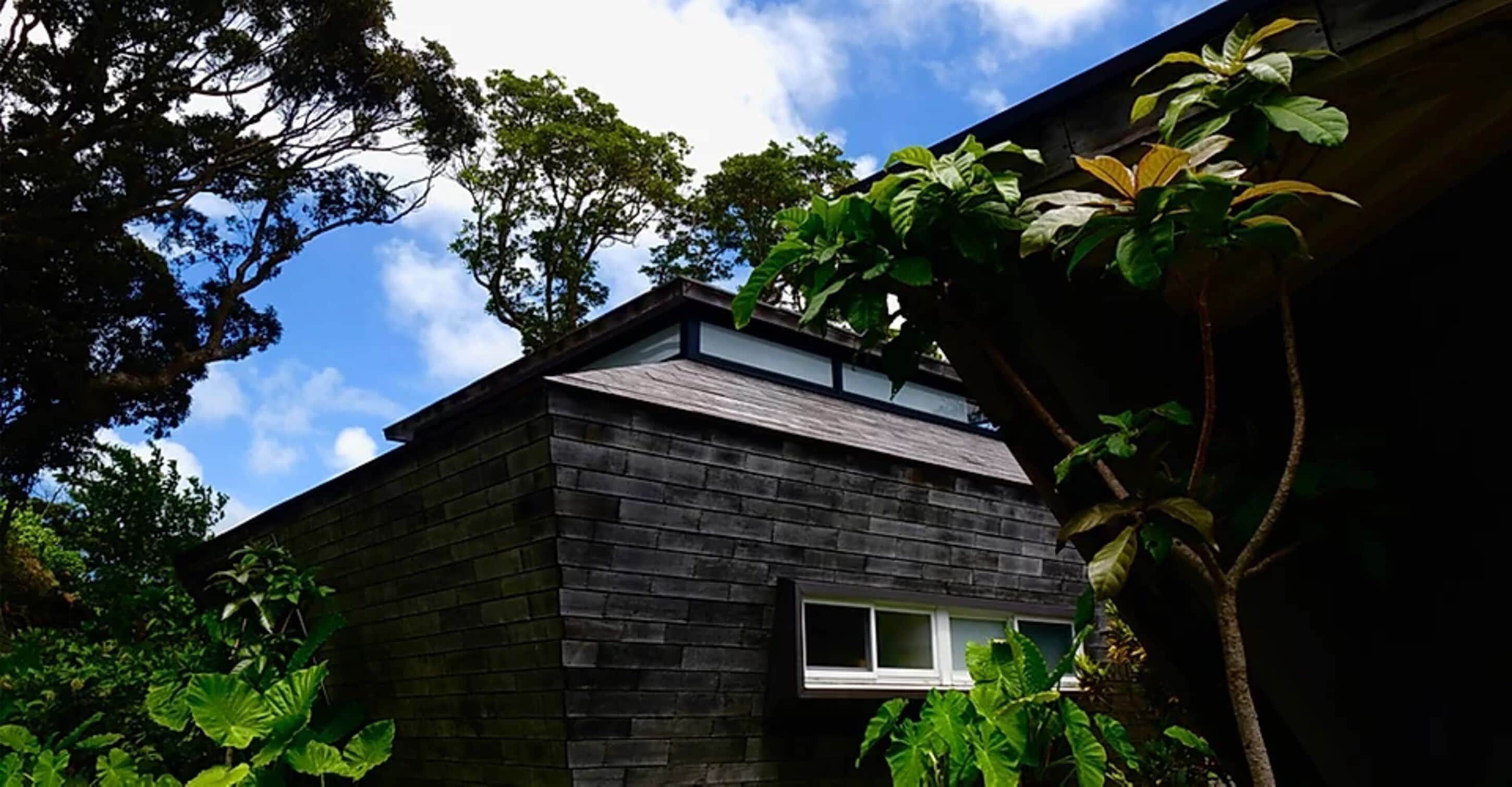 Una casa moderna con fachada de ladrillo oscuro, techo inclinado y una ventana pequeña.