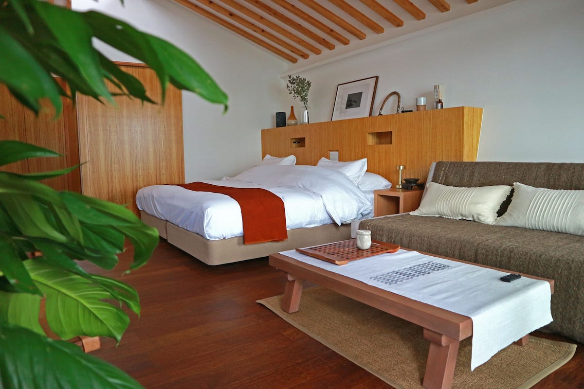 A bedroom with a bed, a bedside table, a nightstand, a sofa, and a wooden ceiling.