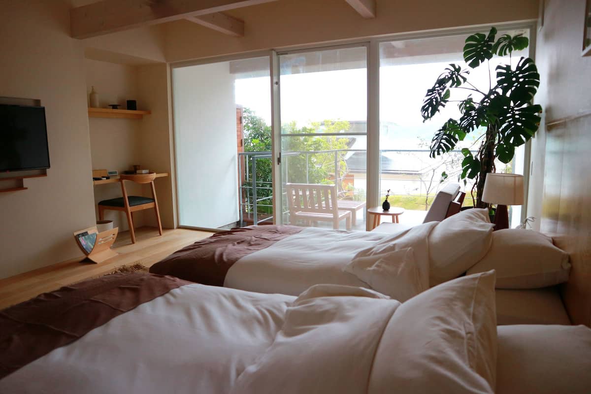 A bedroom with two beds, a TV, a desk, and a balcony with a chair.