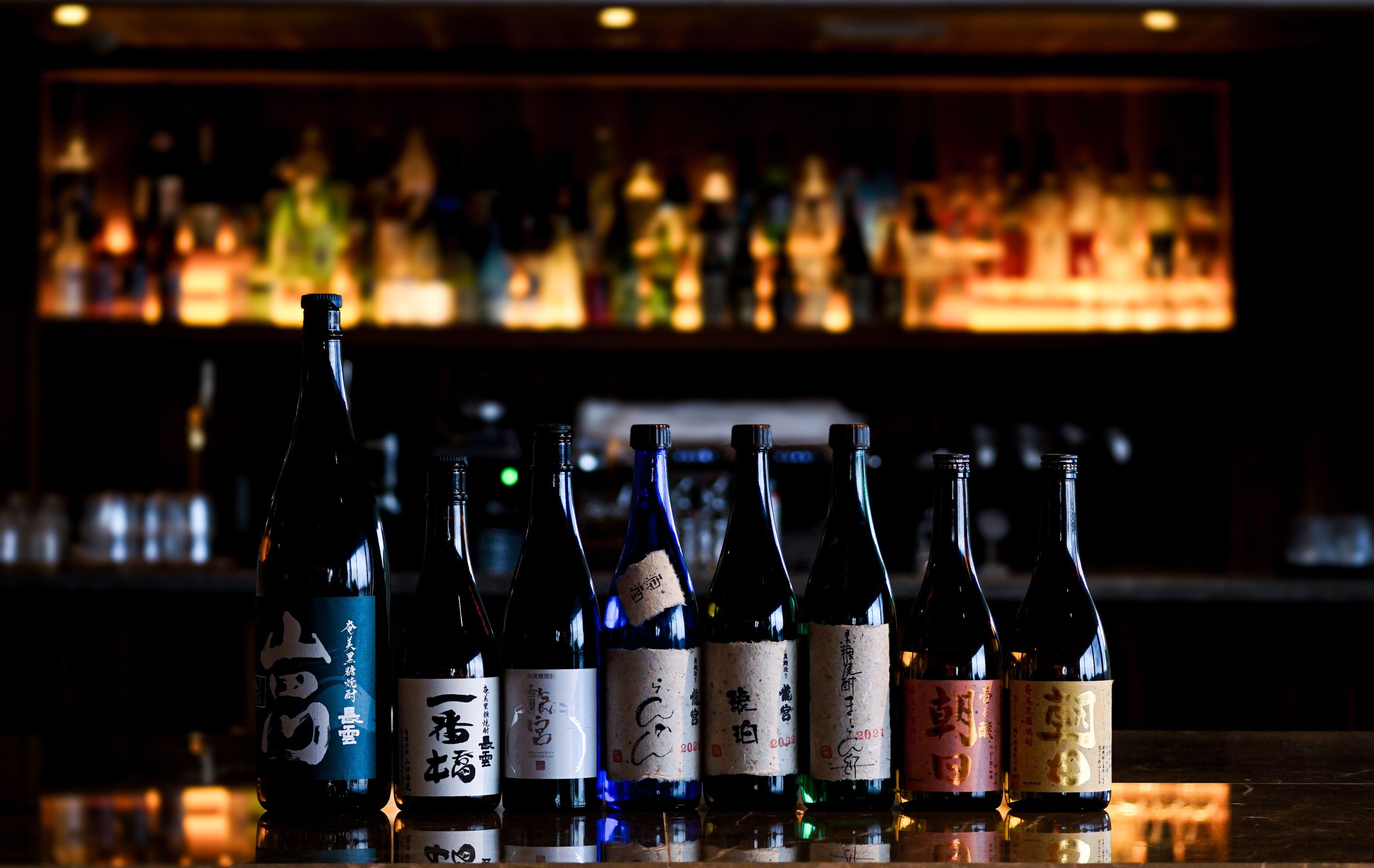 Un bar où l’on peut voir plusieurs bouteilles de saké alignées sur le comptoir.
