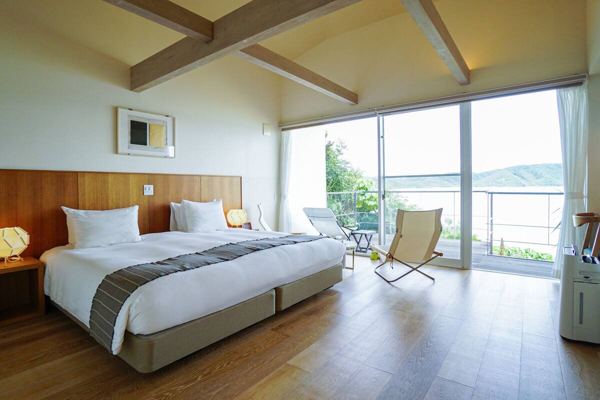 A spacious bedroom with a large bed, a chair, and a balcony with a view of the outdoors.