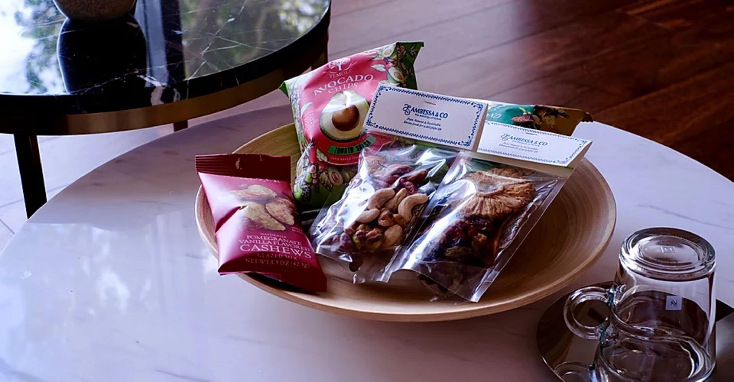 Ein Tisch mit einer Schale Snacks, darunter Cashewnüsse und Avocado-Chips, sowie einer Glas-Tasse.