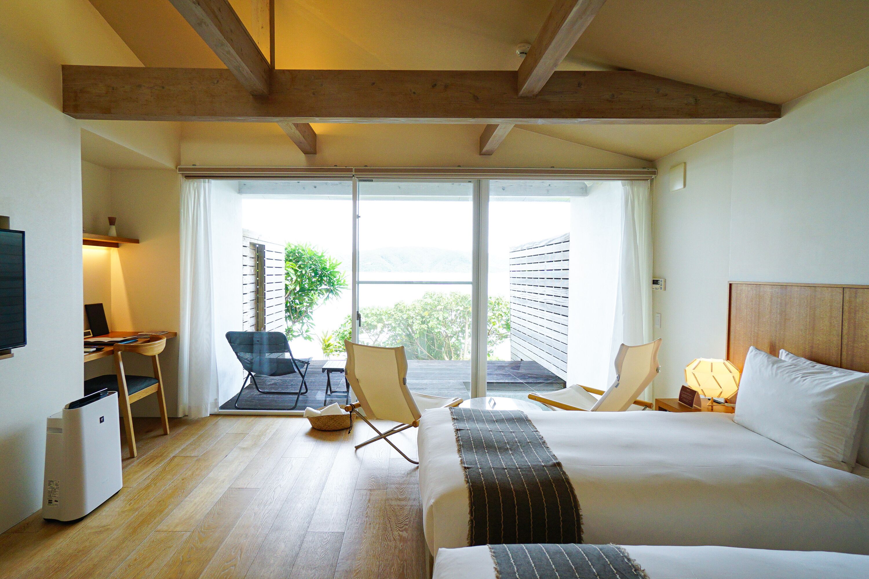 Habitación de hotel con cama, escritorio, silla, televisor y balcón con vistas.