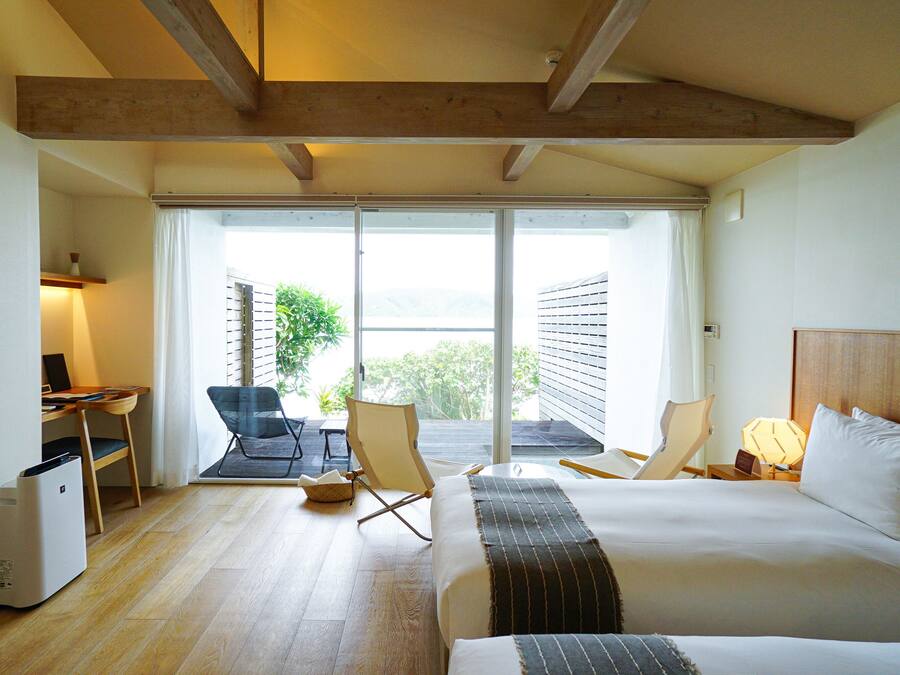 Habitación de hotel con cama, escritorio, silla, televisor y balcón con vistas.
