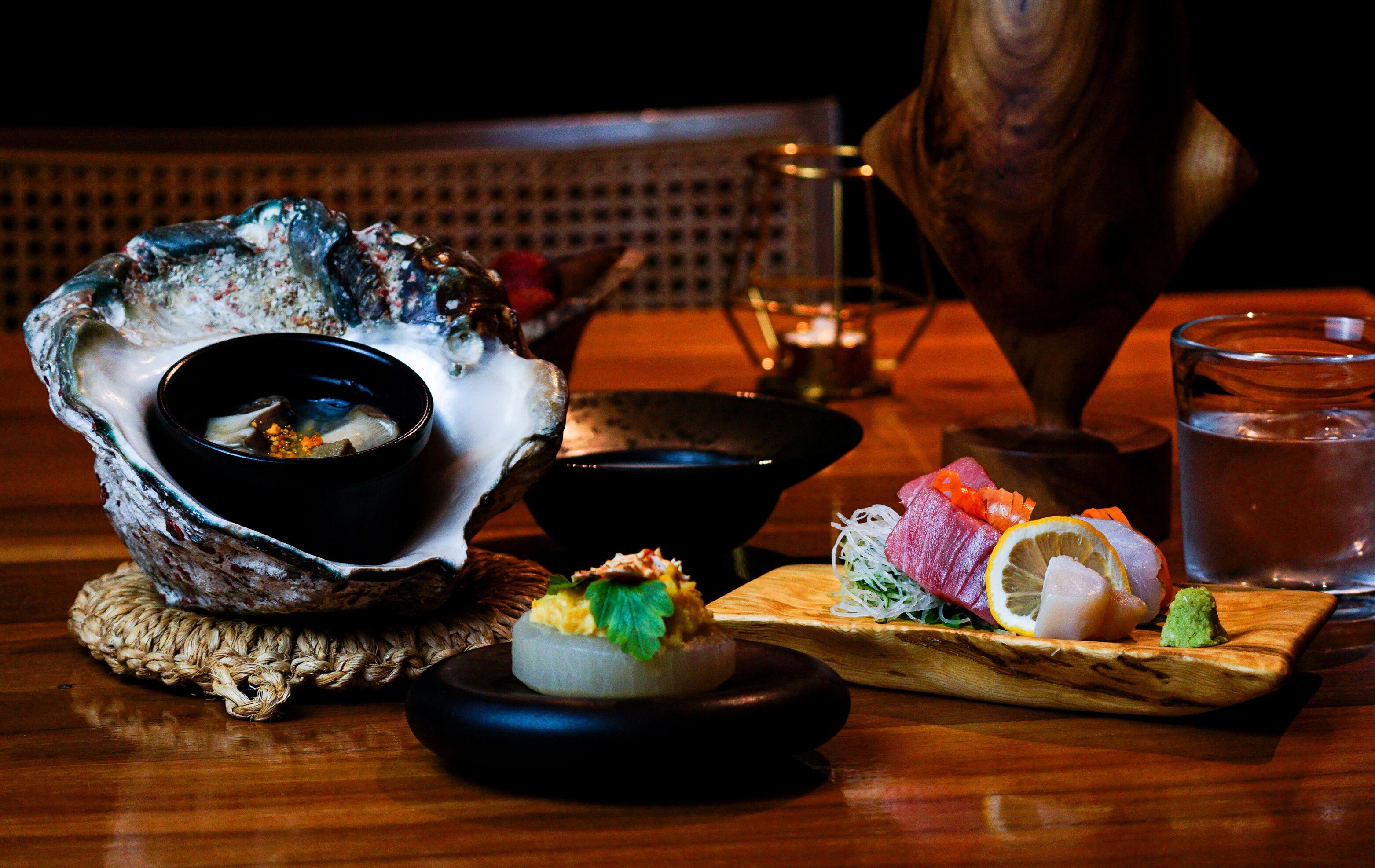 A wooden table with a variety of dishes, including sushi and sashimi, and a bowl of soup.