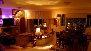 A cozy living room with a fireplace, a sofa, a coffee table, and a dining area with chairs. - Villa Paradizo (Kalamata)