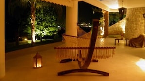 A hammock in a well-lit room with a view of a tree and a stone wall. - Villa Paradizo (Kalamata)
