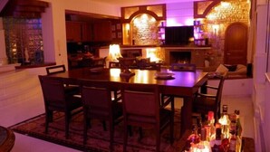 A dining area with a large wooden table, chairs, and a bar with bottles. - Villa Paradizo (Kalamata)